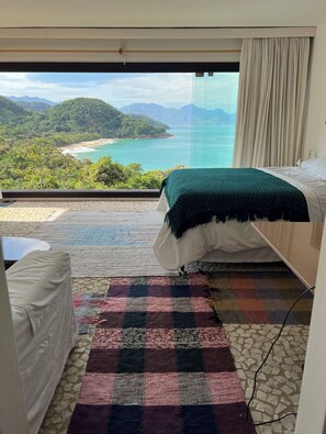 Un dormitorio con cama, una mesita, alfombra colorida y vistas a la playa y montañas.