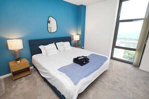 Ett hotellrum med en stor säng, två sänglampor, en spegel och utsikt över staden genom ett stort fönster.