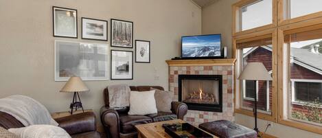 A cozy living room with a fireplace, leather furniture, and framed pictures on the wall.