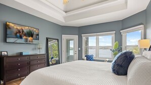 Une chambre à coucher avec un grand lit, un téléviseur fixé au mur, une commode et une fenêtre donnant sur un beau paysage.