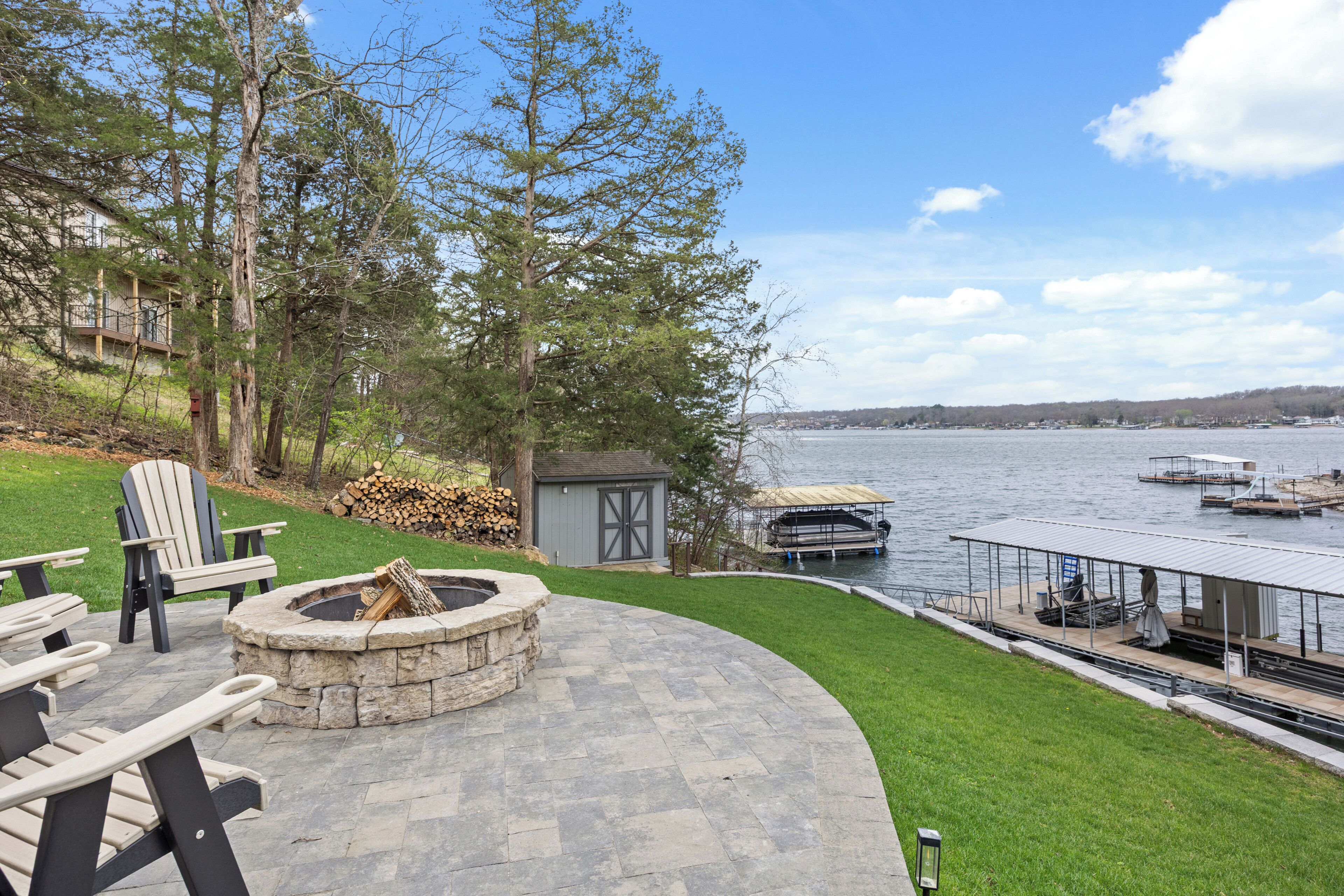 Une terrasse avec des sièges d’extérieur, un foyer, un abri de jardin et une vue sur un lac avec des quais.
