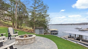 Une terrasse avec des sièges d’extérieur, un foyer, un abri de jardin et une vue sur un lac avec des quais.