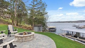 Une terrasse avec des sièges d’extérieur, un foyer, un abri de jardin et une vue sur un lac avec des quais.