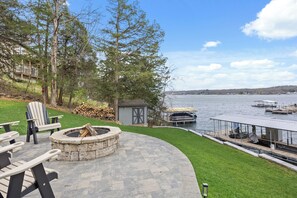 A patio with outdoor seating, a fire pit, a shed, and a view of a lake with docks. - 4BR Lakefront Home, 211’ Shoreline, Sunset Views, 4 MM on the Gravois Arm. (Rocky Mount)