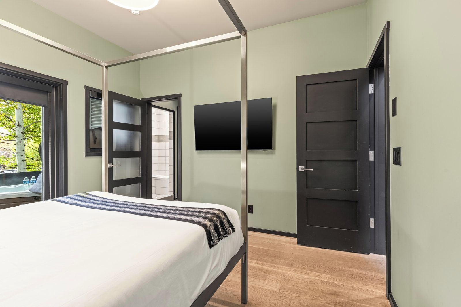 Un dormitorio moderno con cama, televisor, armario y puerta que da a un baño.