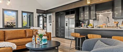 Una cocina moderna con electrodomésticos de acero inoxidable, un comedor con una mesa redonda y sillas, y una sala de estar con sofá y mesa de centro.