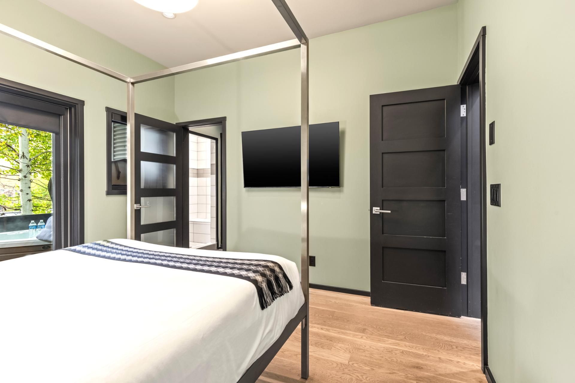 Ein modernes Schlafzimmer mit Bett, Wand-Fernseher und einer Tür zum Balkon.