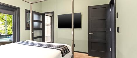 Ein modernes Schlafzimmer mit Bett, Wand-Fernseher und einer Tür zum Balkon.