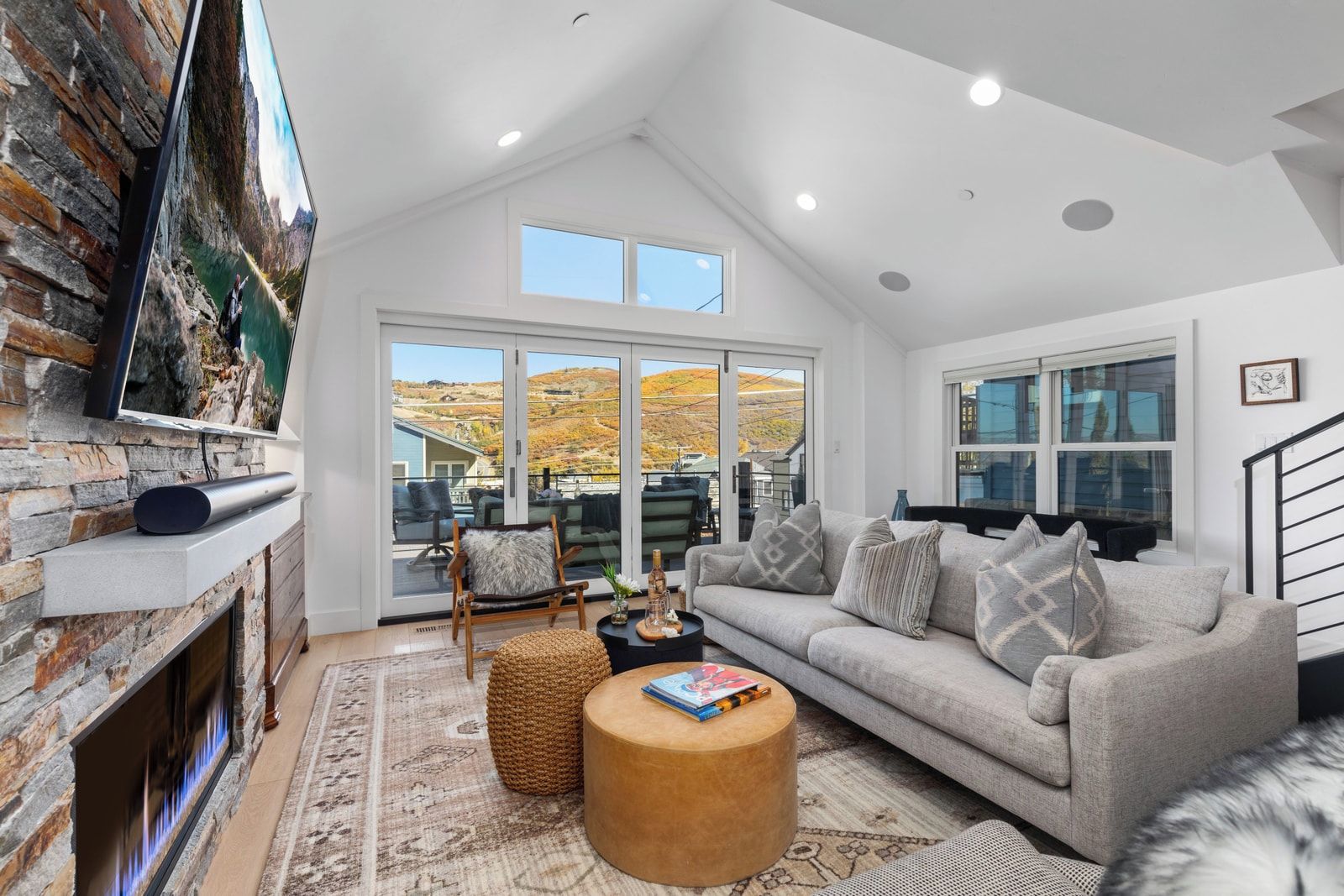 A modern living room with a stone fireplace, a grey sofa, a round wooden coffee table, and a large TV mounted on the wall.