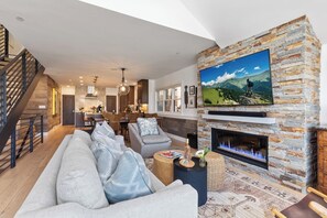 Ein modernes Wohnzimmer mit Kamin aus Stein, einem großen Flachbildfernseher und einer Treppe, die in den oberen Bereich führt.