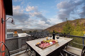 Eine Dachterrasse mit Esstisch, einer Weinflasche und einem schönen Blick auf Hügel und einen bewölkten Himmel.