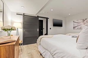 Une chambre d’hôtel moderne dotée d’une porte coulissante, d’un téléviseur à écran plat, d’un lit avec une literie blanche, d’un bureau avec une lampe et d’une fenêtre donnant sur un arbre.