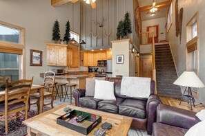 A spacious living room with a leather sofa, a coffee table, and a dining area with wooden chairs and a table. - Walk to Ski Slopes + Trails! 2 Mountain View Homes, 7 Bedrooms, with Private Hot Tubs, Fireplaces, and AC | ML-3981 by KBM (Park City)