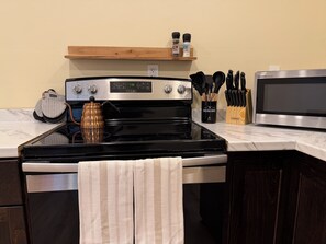 Une cuisine équipée d’une cuisinière, d’un four à micro-ondes et d’une étagère en bois où sont rangées les épices.