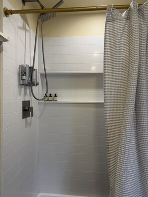 Un espace douche équipé d’un pommeau de douche à main, d’un porte-serviettes et d’une étagère pour les articles de toilette.
