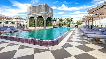 Un espace piscine avec un sol à carreaux, des chaises longues et des parasols.