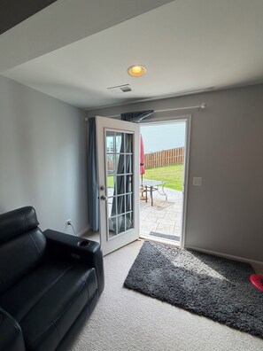 A room with a black leather sofa, a grey carpet, a sliding glass door leading to a patio with a table and chairs, and a red umbrella. - Cozy 2-bedroom basement in charming Gainesville (Gainesville)