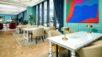 Un hall d’hôtel moderne doté d’un espace repas, de grandes fenêtres et d’un tableau abstrait aux couleurs vives.