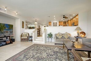 Uma sala de estar ampla com televisão de tela plana, um sofá, uma mesa de centro e um espaço de refeições com cadeiras.