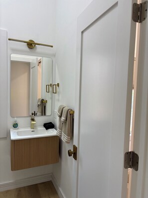 A bathroom with a white sink, a mirror, a towel rack, and a door with a gold handle.