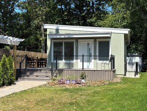 A small, single-story building with a porch, a covered outdoor seating area, and a fenced yard. - Modern Beach Cottage (Sag Harbor)