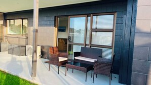 Un patio cubierto con mobiliario de mimbre, una puerta corrediza de vidrio y vistas al exterior.