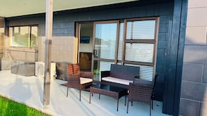 Un patio cubierto con mobiliario de mimbre, una puerta corrediza de vidrio y vistas al exterior.