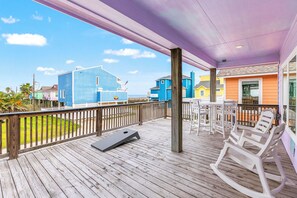 Une terrasse en bois avec un trampoline, des chaises blanches et une vue sur des bâtiments aux couleurs vives.