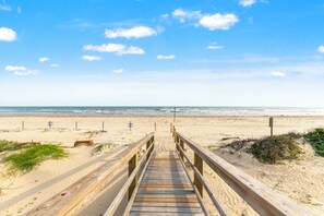 Une promenade en bois mène à une plage de sable fin, sous un ciel dégagé.