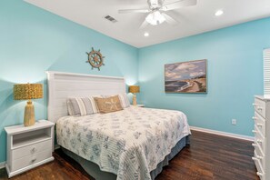 Une chambre à coucher comprenant un lit, des tables de chevet, un ventilateur de plafond, une horloge murale et un tableau.