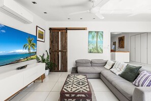A modern living room with a large TV, a grey sofa, a patterned rug, and a wooden door.