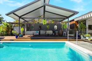 A modern outdoor pool area with a covered patio, seating, and potted plants.