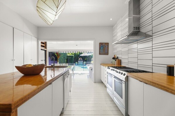 A modern kitchen with white cabinetry, a wooden countertop, a built-in oven, and a view of a pool.