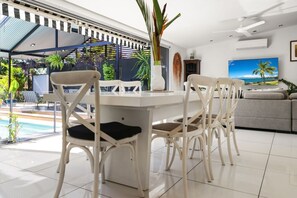 A modern living room with a dining table, white chairs, a sofa, and a TV.