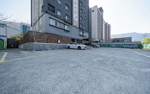 Um estacionamento com um carro branco estacionado perto de um edifício com uma placa que diz 'ABERTO'.