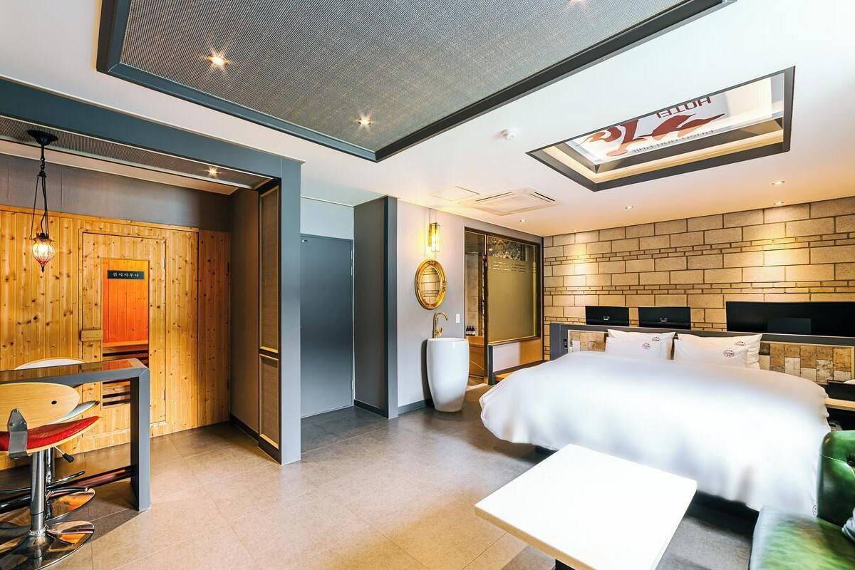 Una habitación de hotel moderna con una cama grande, un escritorio con silla, un espejo amplio y un televisor montado en la pared.