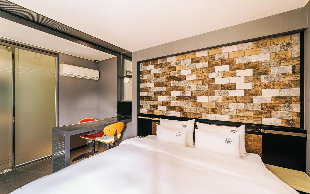 A hotel room with a bed, a desk, a chair, and a wall with a textured pattern.