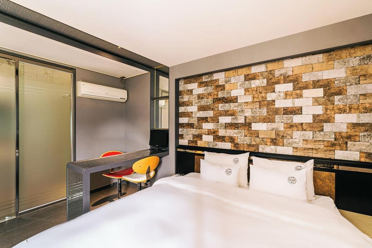 Una habitación de hotel con cama, escritorio, silla y pared con textura.