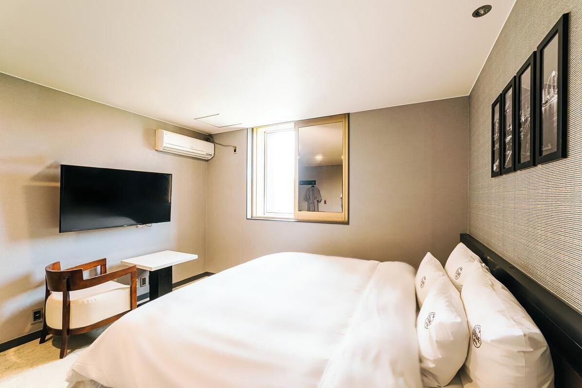 Habitación de hotel con cama, escritorio, silla, televisor y espejo.