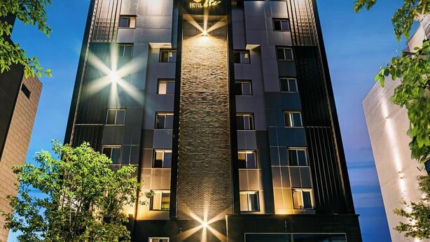 Ein modernes Hotelgebäude mit einer zentralen vertikalen Lichtinstallation, zahlreichen Fenstern und einer Ziegelverkleidung.