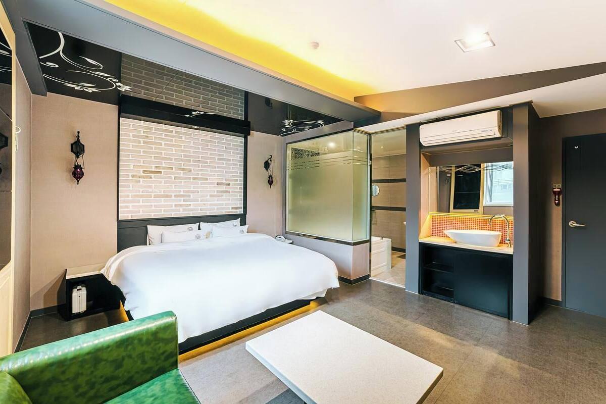 Una habitación de hotel moderna con una cama grande, un baño independiente con un espejo y una silla verde.