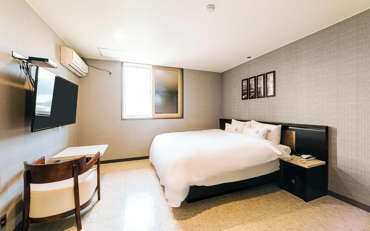 Una habitació d'hotel amb un llit, escriptori, cadira, televisió i finestra.