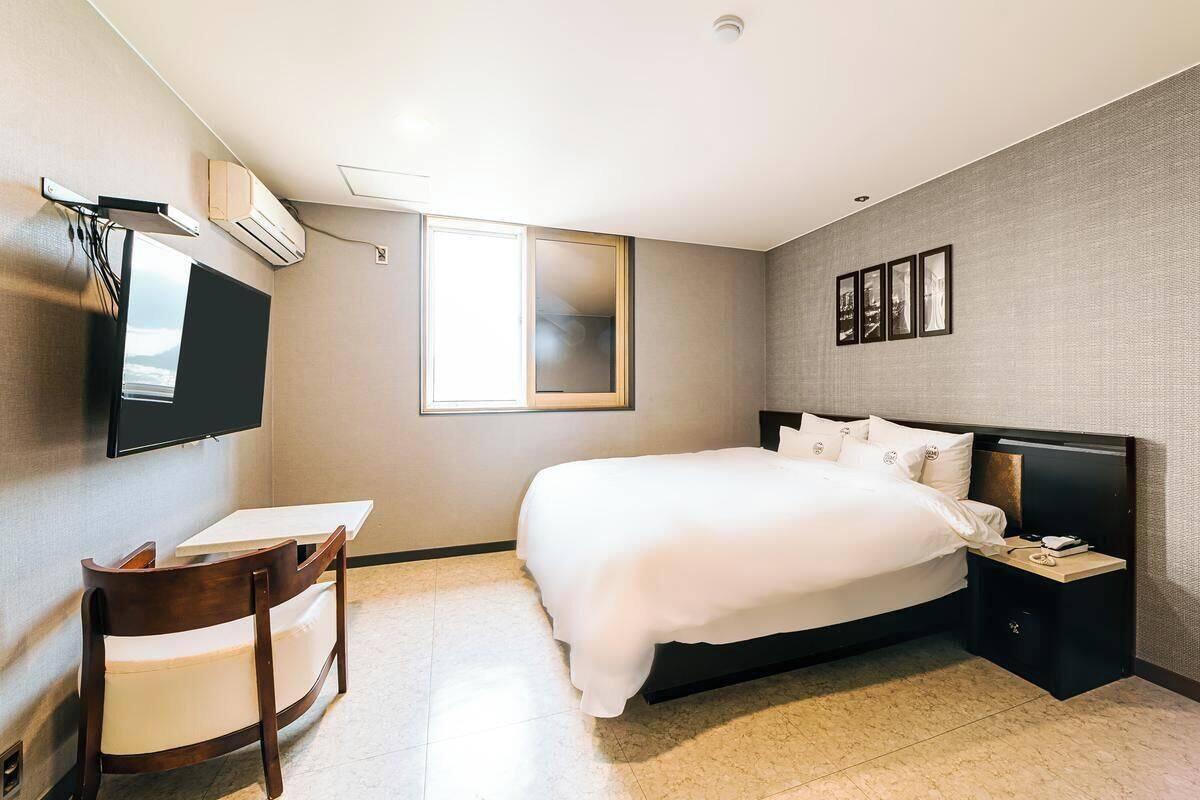 Una habitación de hotel con cama, escritorio, silla, televisor y ventana.