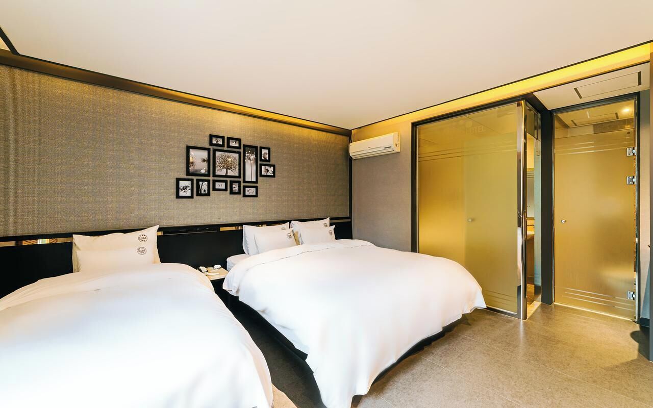 A hotel room with two beds, a wall-mounted picture display, a sliding door closet, and an air conditioning unit.