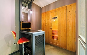 A room with a wooden wardrobe, a desk with a computer, and a red chair.