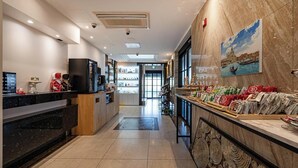 Eine Hotelhalle mit einer Rezeption, einer Kaffeemaschine, einem Fernseher und einer Wand mit einem Gemälde.