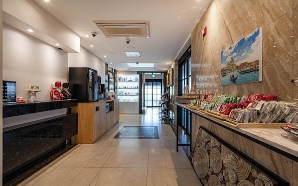 A hotel lobby with a reception desk, a coffee machine, a TV, and a wall with a painting.