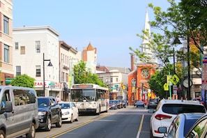 A street view with parked cars, a bus, and buildings with commercial signs.