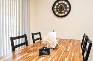 Una mesa de comedor con un reloj en la pared, sillas y un cartel decorativo.