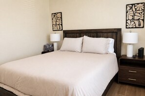 A neatly made bed with a wooden headboard, two bedside tables with lamps, and wall art. - Roomy 3BR & 2BA Retreat with Laundry & King Bed (Hanford)